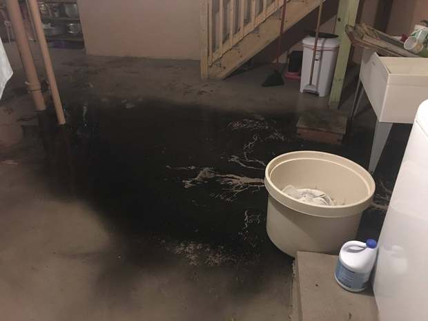 Black sewage water spreading across a flooded Chicago basement floor near the stairs