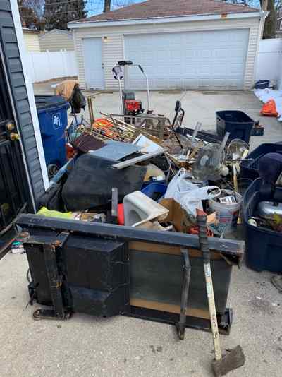 Pile of household junk and old appliances staged in a driveway for pickup in Chicago